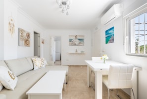 A modern living room with a sofa, a dining table, and a kitchen area in the background. - Andalusian Home with Pool, Rooftop Terrace "Love under the Stars" & Mountain View (Sayalonga)