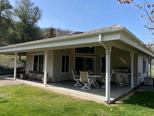 Un patio couvert avec des meubles d’extérieur, un barbecue et une fenêtre donnant sur une pelouse.