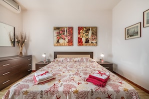 A bedroom with a bed, two bedside tables, a dresser, and two wall-mounted paintings.