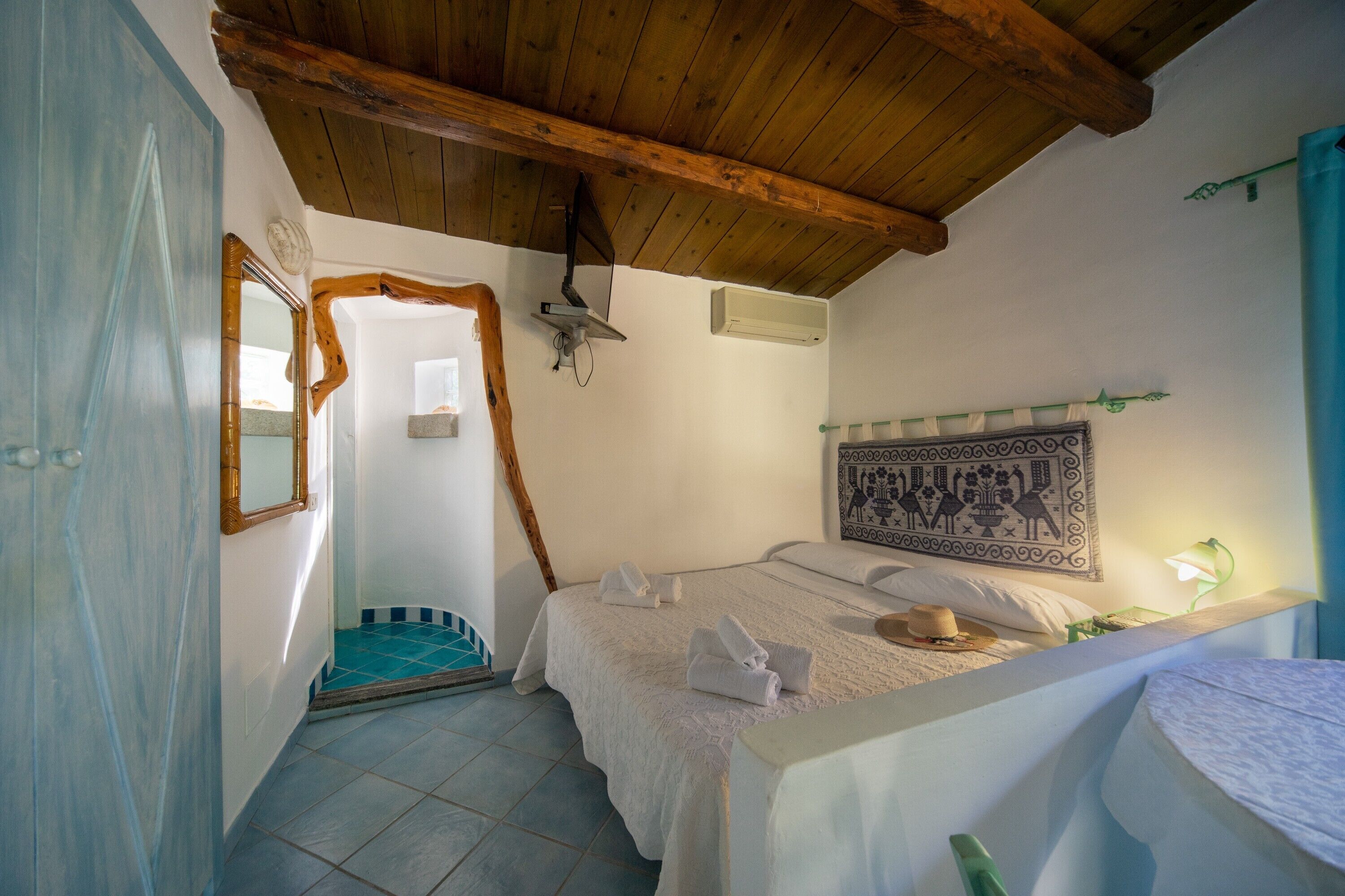 Une chambre avec un plafond en bois, un lit avec une literie blanche, un climatiseur fixé au mur et une tapisserie à motifs.