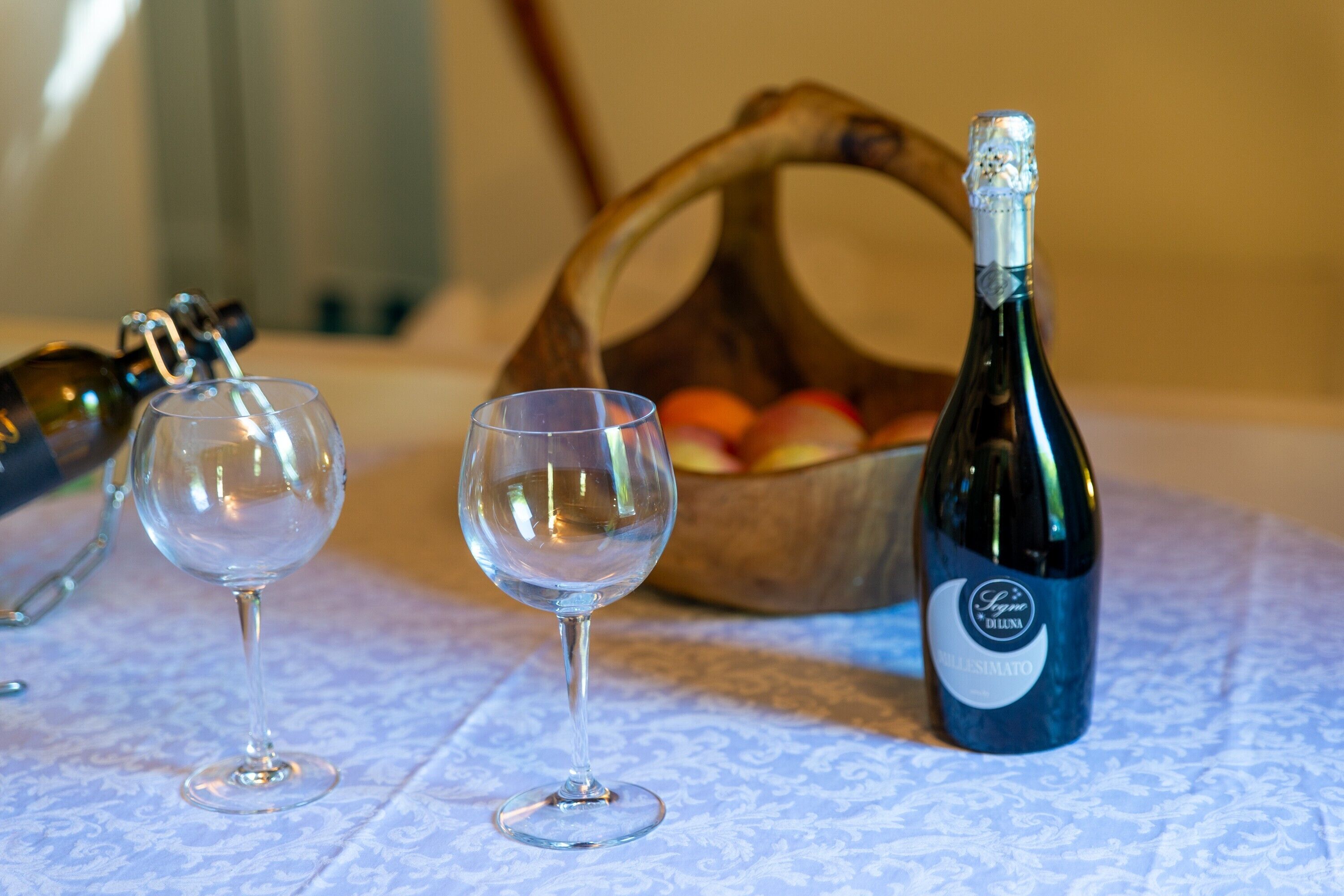 A table with two wine glasses, a bottle of wine, and a basket of fruit.