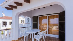 A balcony with a white table and chairs, a view of a building, and a tiled floor. - Family Villa with Sea Views (San Jaime Mediterráneo)