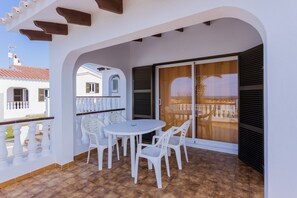 A balcony with a white table and chairs, a view of a building, and a tiled floor.