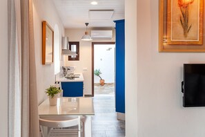 A modern kitchen with a glass table, white chairs, a potted plant, and a TV mounted on the wall.