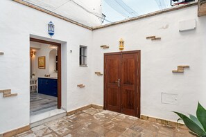 A courtyard with a wooden door, a blue cabinet, and a white wall with a small window.