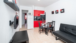 A compact living space with a kitchenette, a dining area with a table and chairs, and a black sofa.