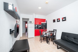 Un espace de vie compact comprenant un coin cuisine, un coin repas avec une table et des chaises, et un canapé noir.