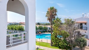 A view of a swimming pool, palm trees, and a building with a white facade.