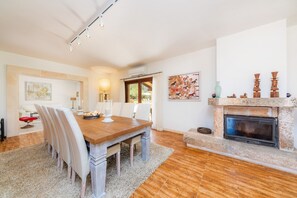 Een eetruimte met een houten tafel en stoelen, een open haard en kunstwerken aan de muur.