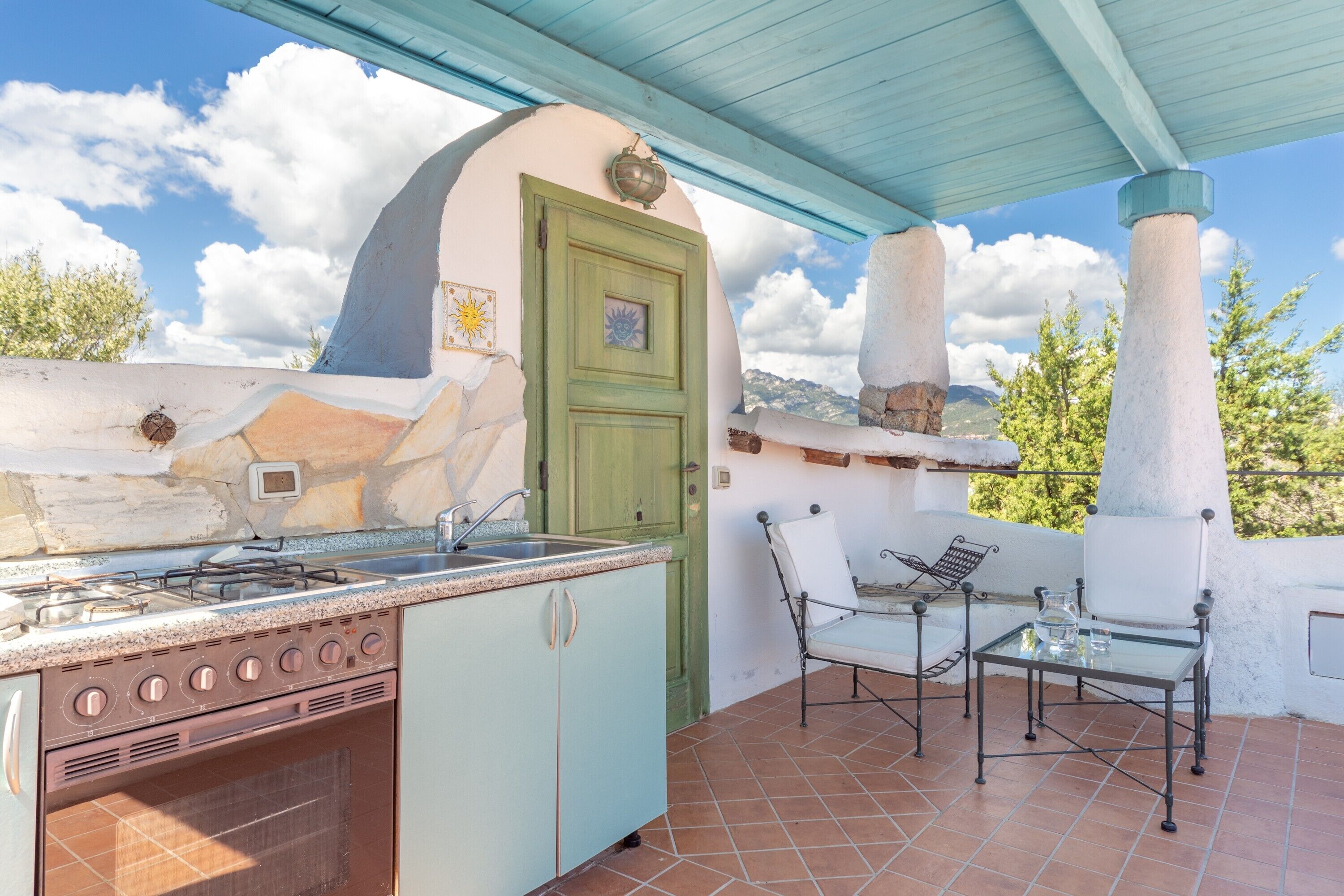 An outdoor kitchen with a gas stove, sink, and a dining area with chairs and a table.