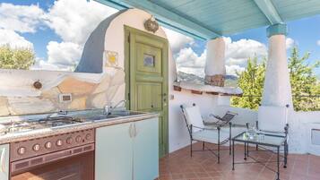 An outdoor kitchen with a gas stove, sink, and a dining area with chairs and a table.