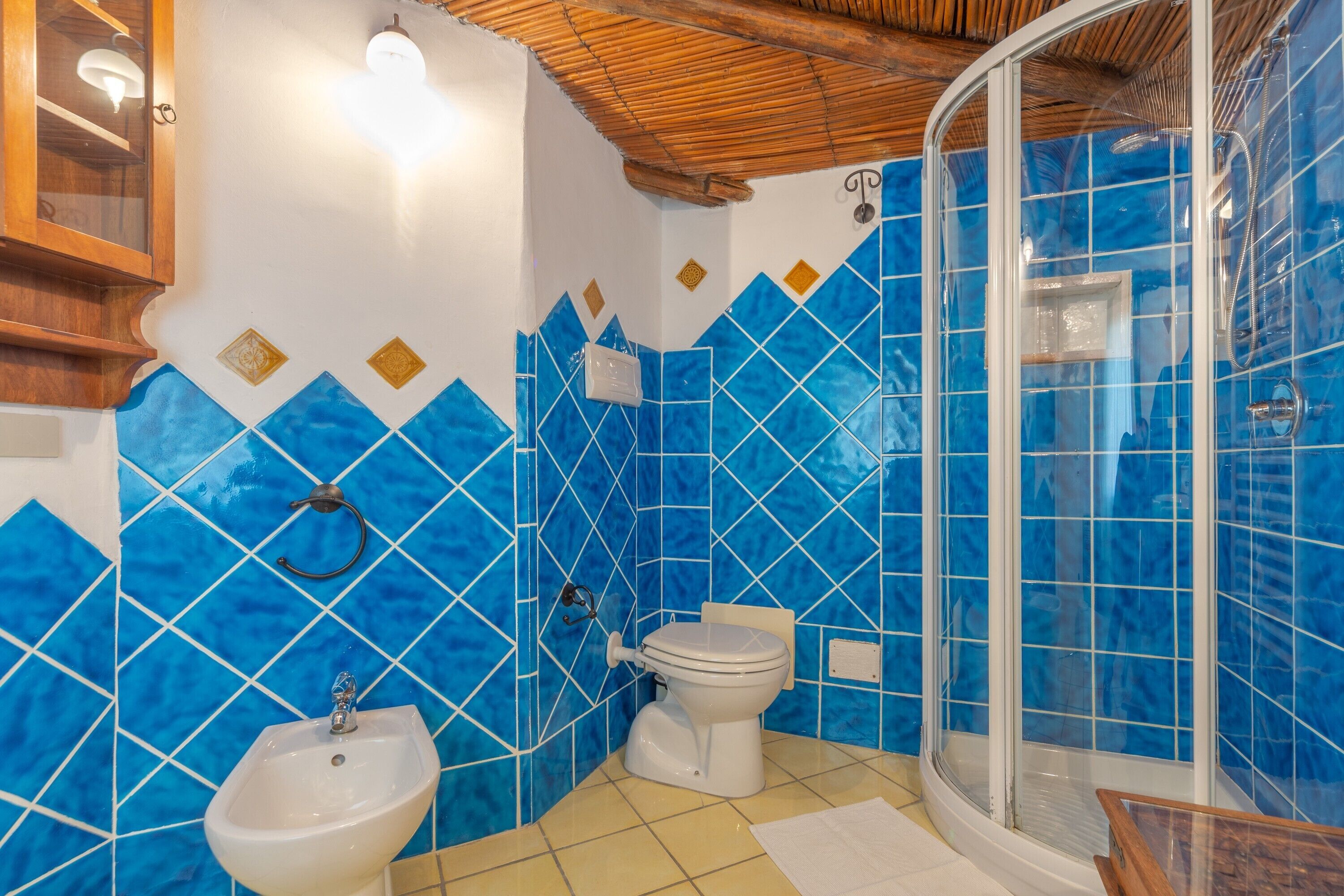 Un baño con paredes de azulejos azules, un lavamanos blanco, un inodoro y una ducha con mampara de vidrio.