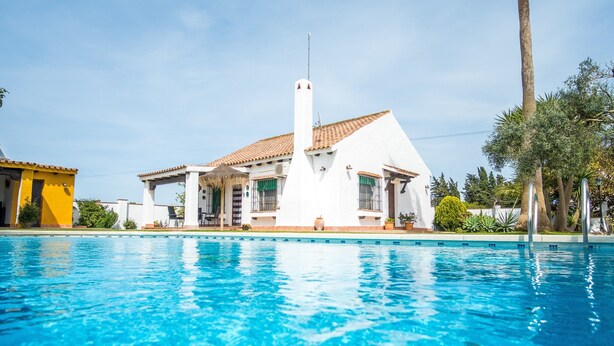 Une maison avec une piscine, une façade blanche et un toit recouvert de tuiles rouges.