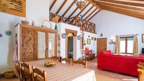 Un espace repas comprenant une table et des chaises en bois, un canapé rouge et un plafond haut avec des poutres apparentes.