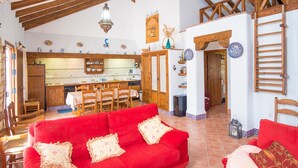 Un vaste espace de vie avec un canapé rouge, des poutres en bois au plafond, une cuisine à l’arrière-plan et un coin repas avec des chaises et une table.