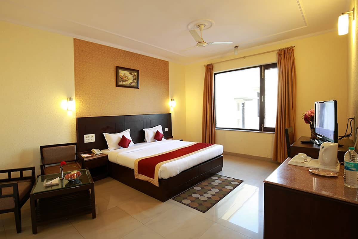 A hotel room with a bed, a desk, a chair, a television, and a window with curtains.