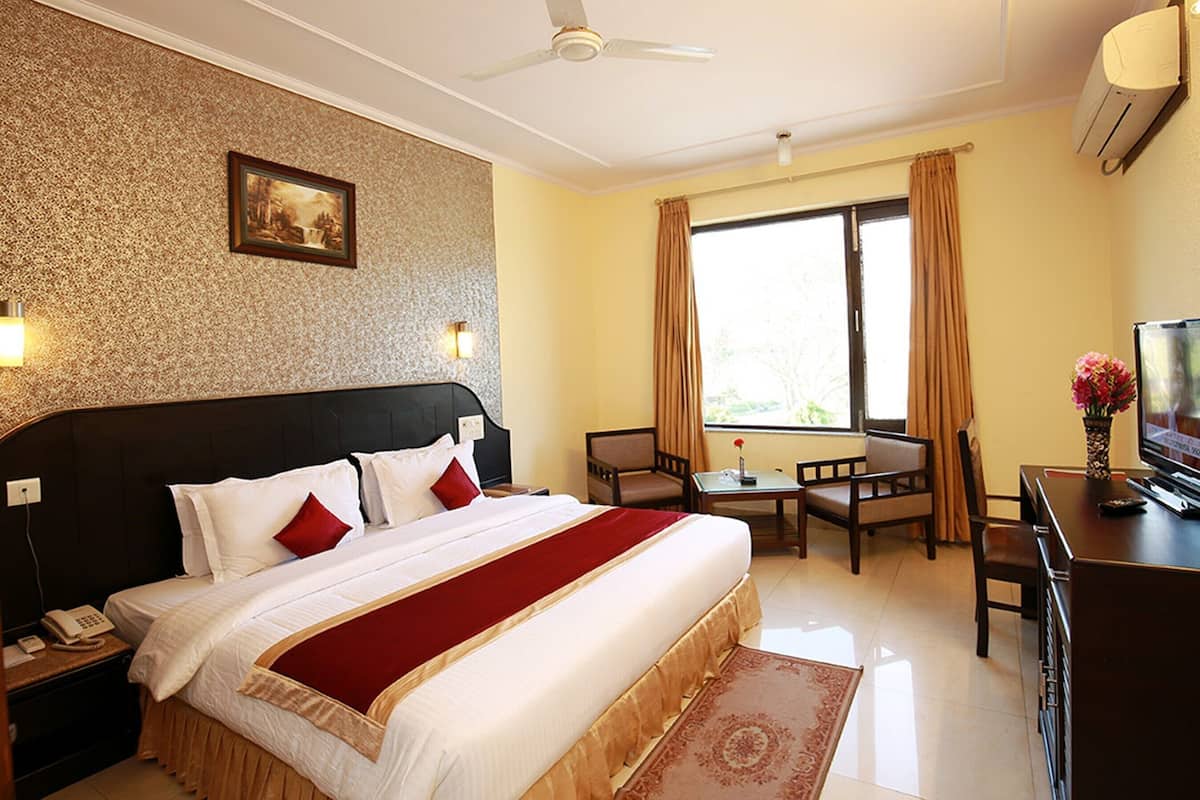 A hotel room with a large bed, a desk with a TV, a chair, a small table, and a window with curtains.
