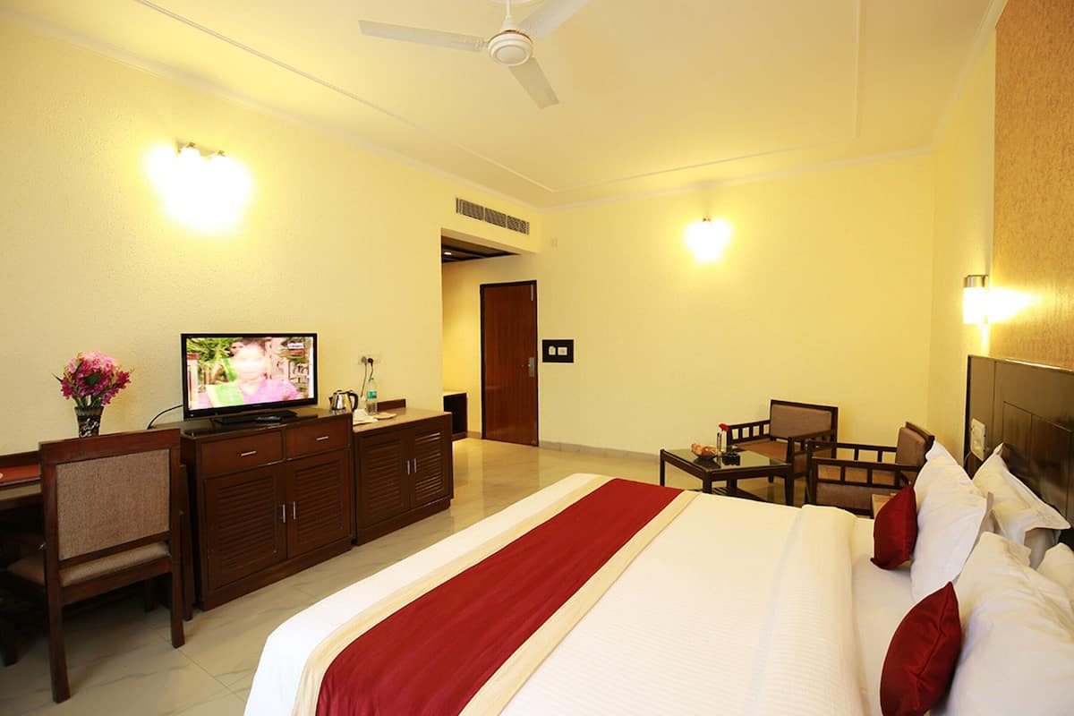 A hotel room with a large bed, a desk with a chair, a television, and a small table with a chair.