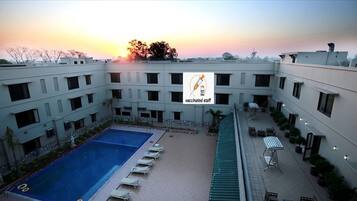 A courtyard with a swimming pool, lounge chairs, and a building with multiple windows.