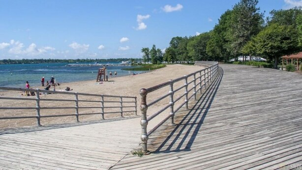 En träpromenad som leder till en strand där det finns folk och ett livräddartorn.
