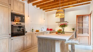 Una cocina con armarios de madera, una isla central, una lámpara colgante y un taburete de bar.