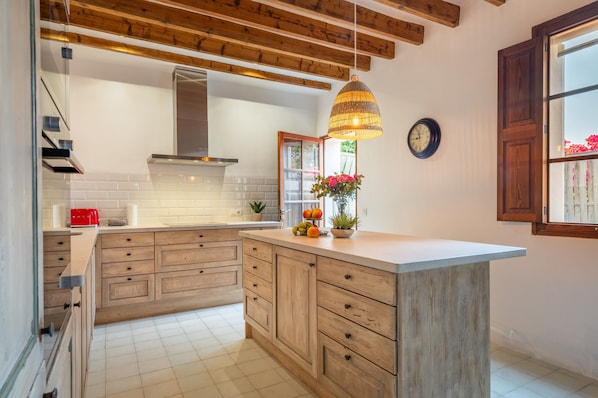 Une cuisine avec des meubles en bois, un plan de travail blanc, un luminaire suspendu et une horloge au mur.
