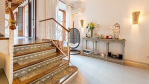 Una escalera con escalones decorados que conduce a una plataforma, una silla, una consola con objetos decorativos y una lámpara fijada a la pared.