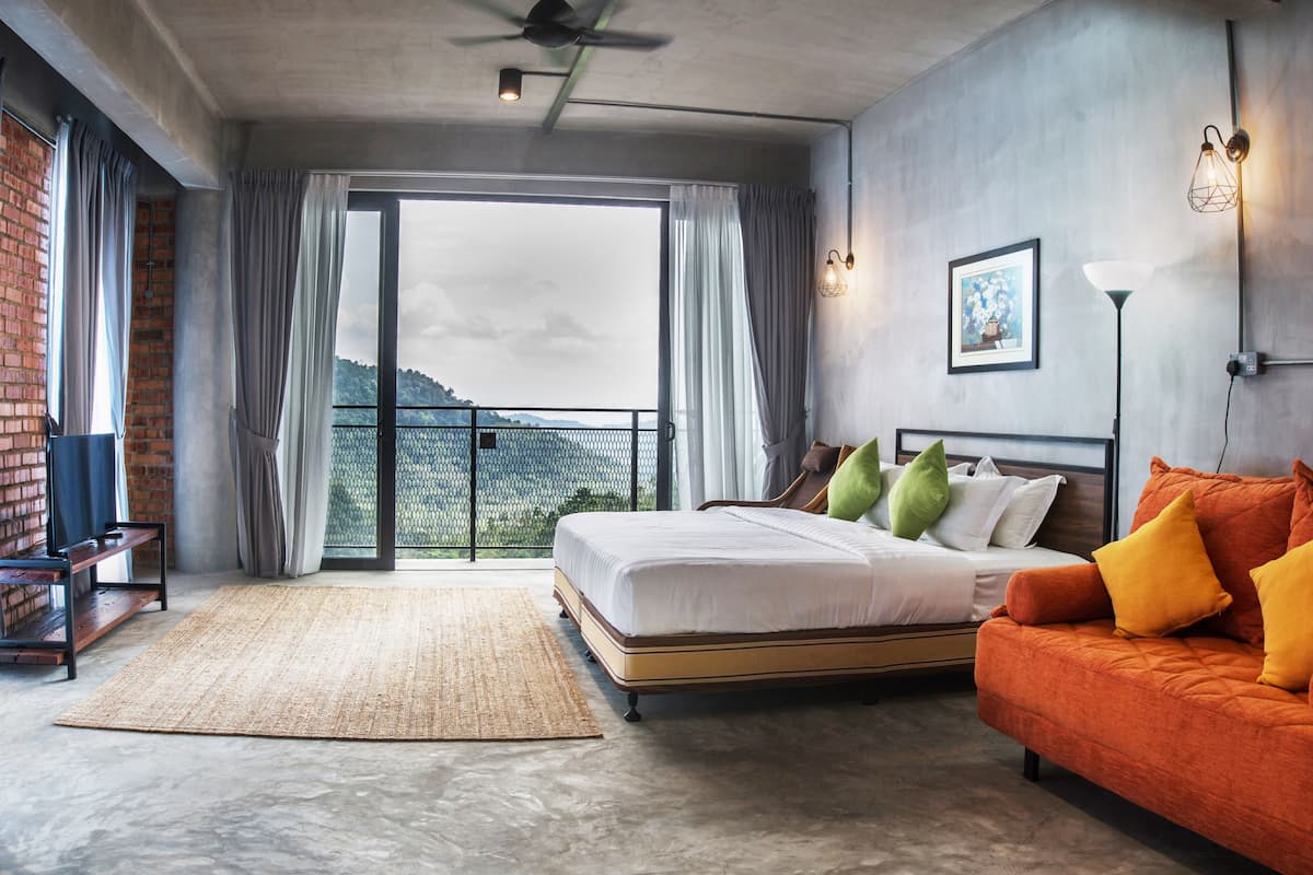 A bedroom with a large bed, a sofa, a view of the outdoors, and a ceiling fan.