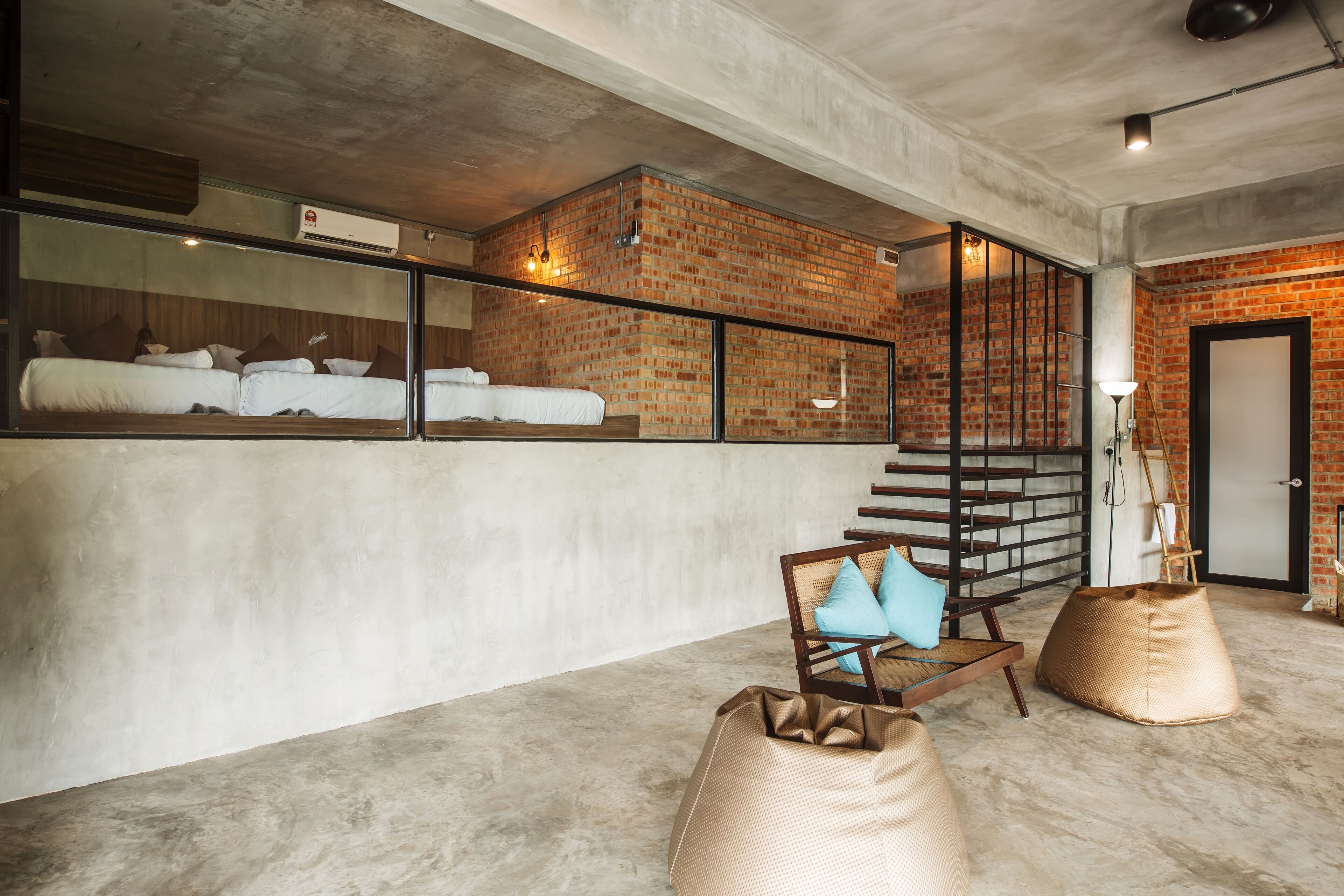 A modern hotel room with a brick wall, a large bed, a wooden chair, and a bean bag.