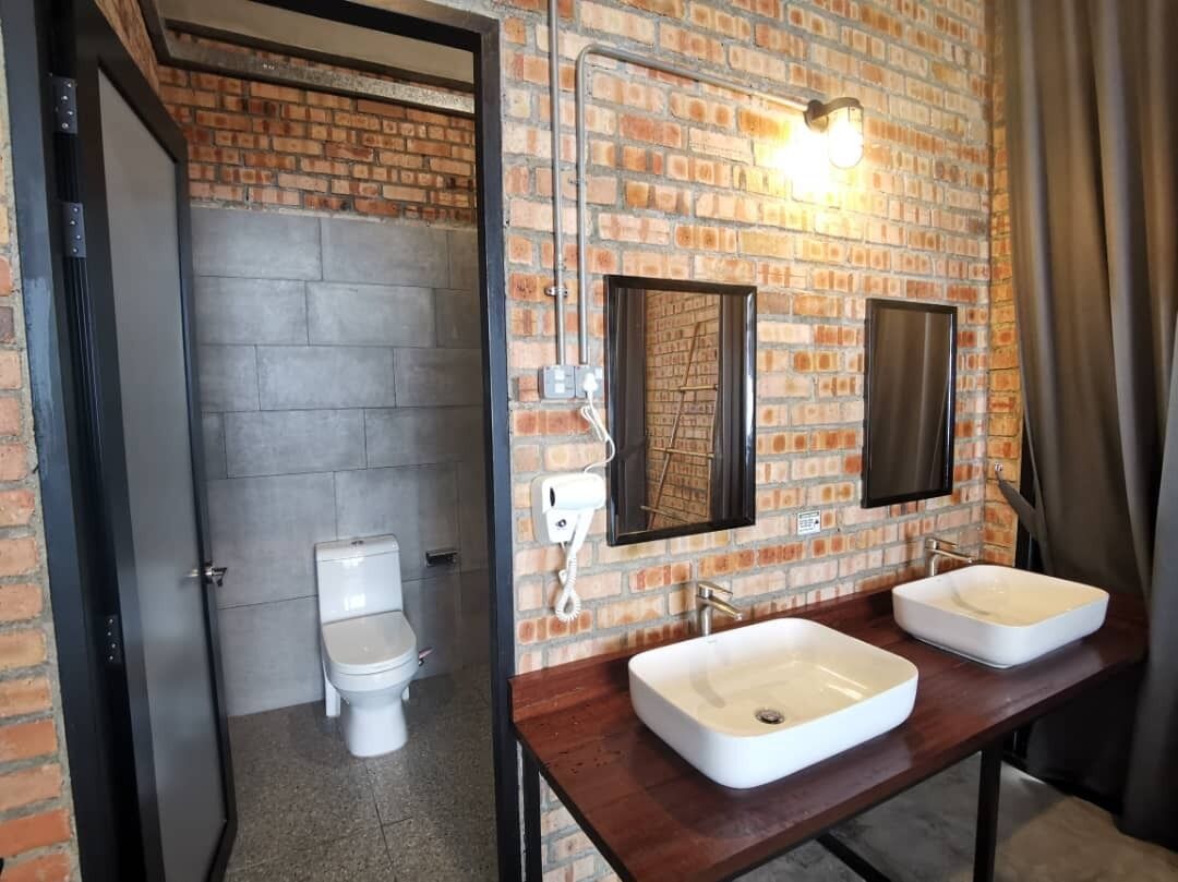 A bathroom with a brick wall, two sinks, a toilet, and a mirror.