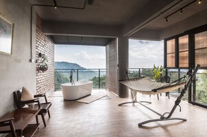 Un balcón amplio con una hamaca, una bañera blanca y una zona de estar con un banco y una mesa.