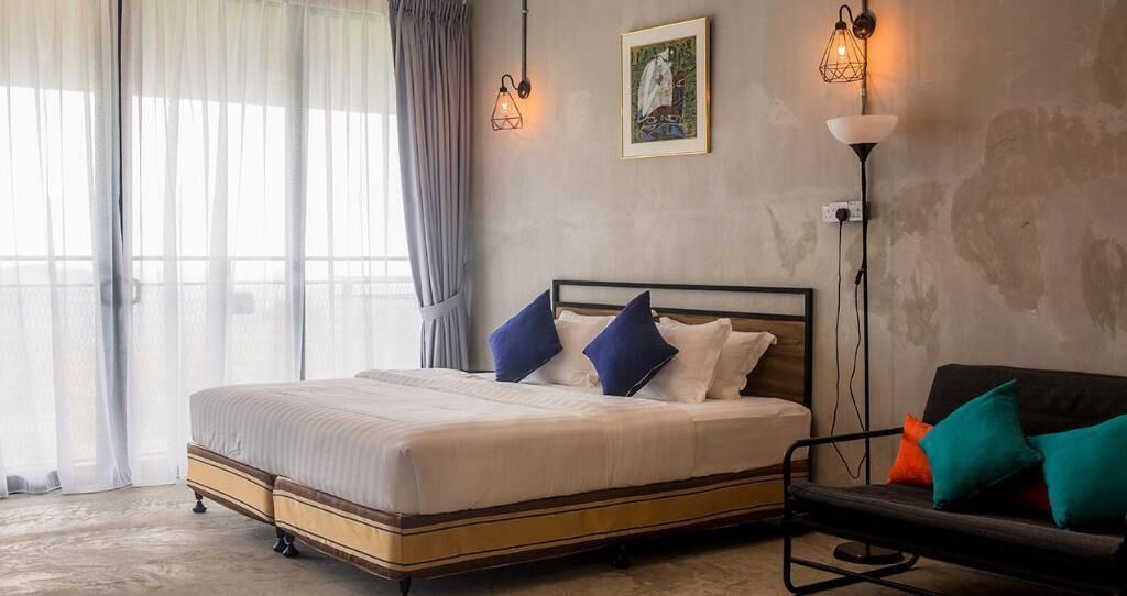 Een slaapkamer met een bed, nachtkastje, stoel en vloerlamp.