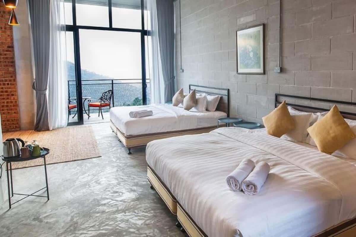 A hotel room with two beds, a view of the sea, a brick wall, and a small table with a chair.