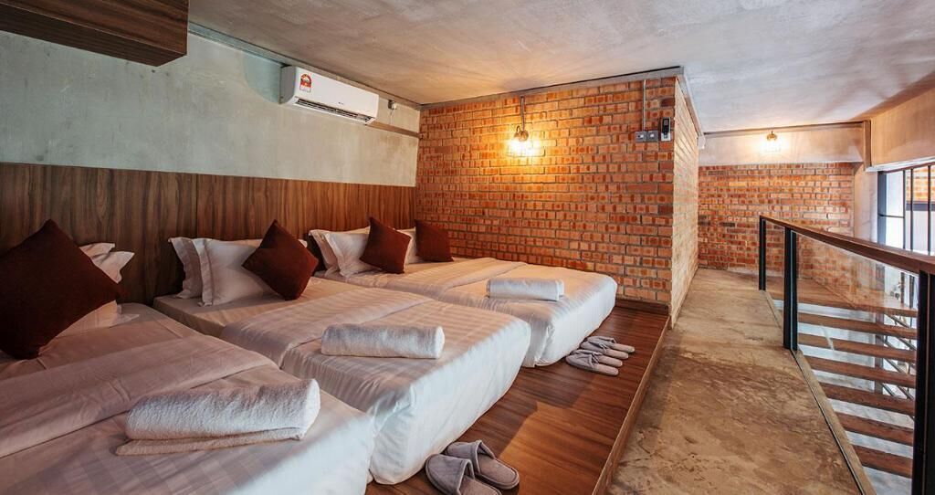 A hotel room with three beds, a brick wall, and a wooden floor.
