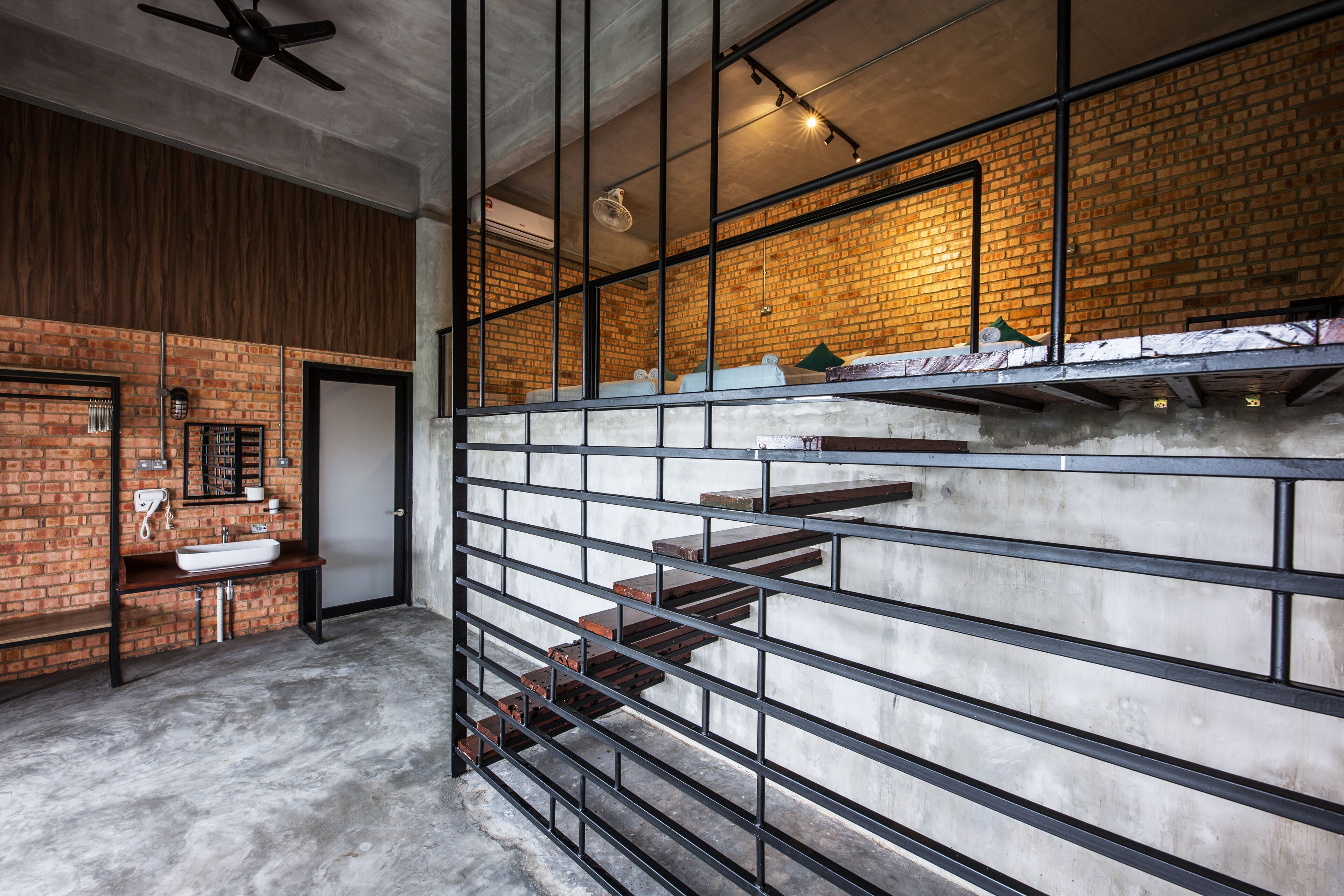 A modern bathroom with a concrete floor, a wooden vanity, a white sink, and a brick wall.