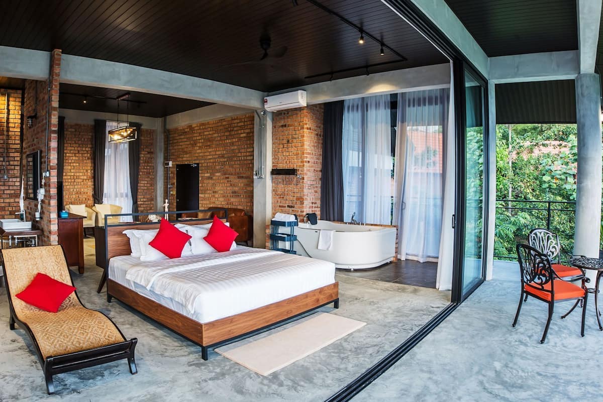 A modern hotel room with a large bed, a sitting area, a bathroom, and a balcony with a view.