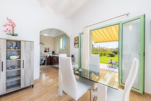 Une cuisine moderne avec des meubles blancs, une table à manger en verre et une vue sur le jardin.