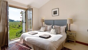 A bedroom with a large bed, a nightstand, a lamp, and a view of a vineyard through an open door. - La Maison – Spacious Country Home with Pool and Lush Garden (Villeneuve de Duras)