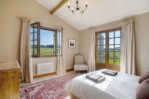 Ein Schlafzimmer mit einem großen Bett, einem Sessel, einer Heizung und Blick auf ein Weinberg durch offene Fenster.