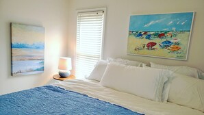 Un dormitorio con una cama, una lámpara y dos cuadros en la pared.