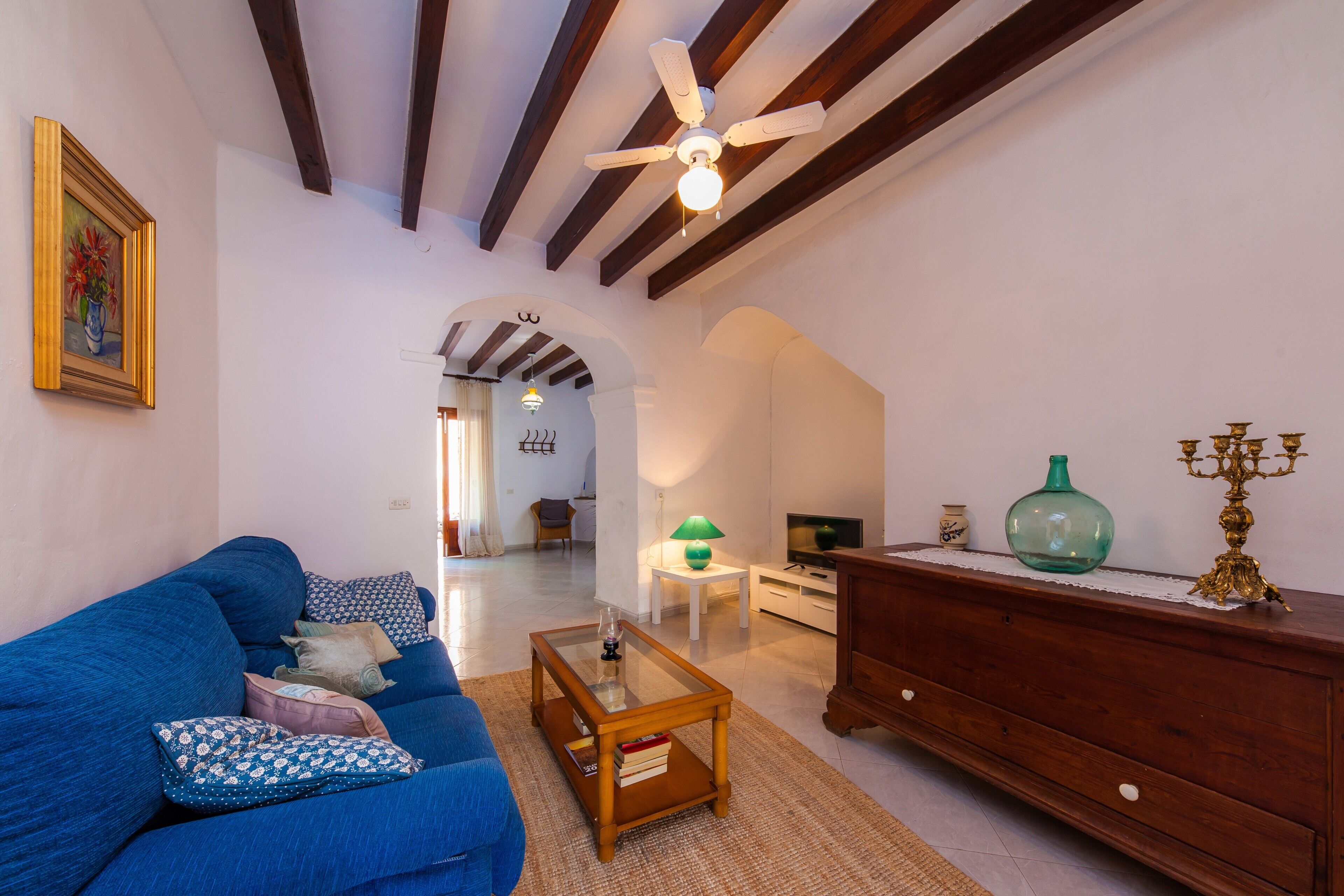 A living room with a blue sofa, a wooden coffee table, a ceiling fan, and a TV on a white stand.