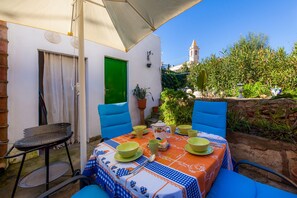 Une terrasse extérieure avec une table dressée pour le repas, une porte verte et, au loin, une vue sur une tour.