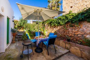 An outdoor patio with a table and chairs, a large umbrella, and potted plants.