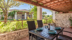 An outdoor patio with a table set for dining, surrounded by stone walls and a view of a house. - Charming Apartment with Beautiful Pool, Jacuzzi, Patio, & Wi-Fi (CONIL DE LA FRONTERA)