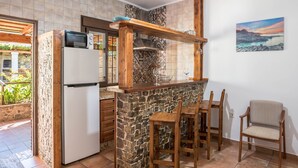 A kitchen with a stone island, wooden chairs, a refrigerator, and a painting on the wall. - Charming Apartment with Beautiful Pool, Jacuzzi, Patio, & Wi-Fi (CONIL DE LA FRONTERA)