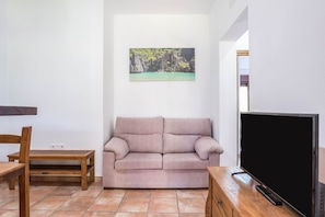 Una sala de estar con un sofá, una mesa de madera, un televisor y un cuadro en la pared.