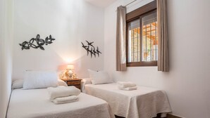 A room with two beds, a window with curtains, a wall decoration, and a bedside lamp. - Charming Apartment with Beautiful Pool, Jacuzzi, Patio, & Wi-Fi (CONIL DE LA FRONTERA)