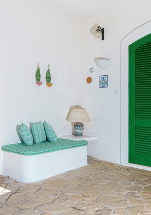 A stone-floored porch with a white bench and a table with a lamp.