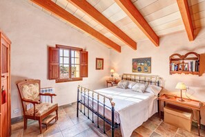 Quarto com cama, cadeira de madeira, mesa de cabeceira e janela com persianas.