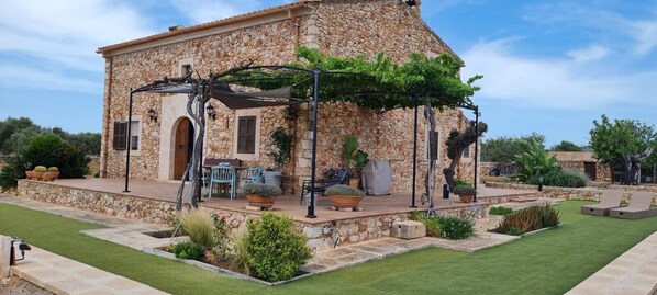 A stone building with a patio, outdoor seating, and potted plants. - Secluded Holiday Home Son Garrot with Garden, Mountain View & Wi-Fi; Parking Available (Santanyí)
